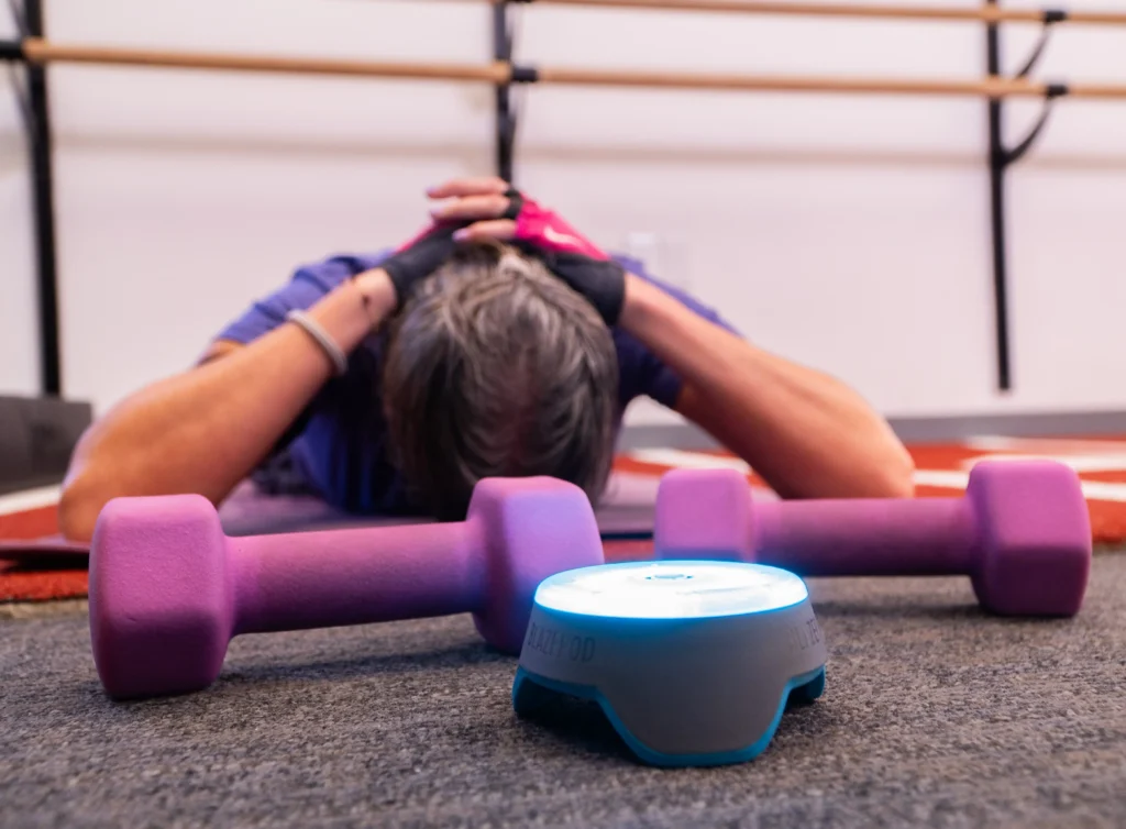 Patient stretching on the floor with dumbbells and a massage device during a neck pain rehabilitation session